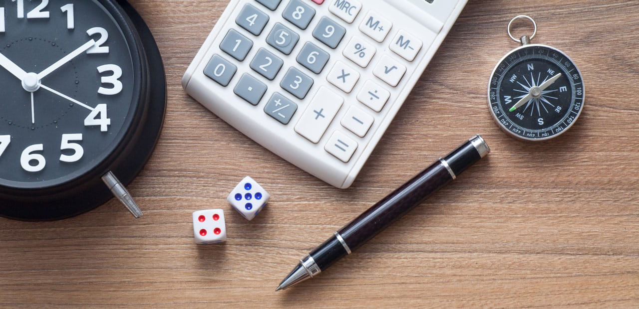 Image containing an alarm clock, a calculator, a compass, a pen and two dice.
